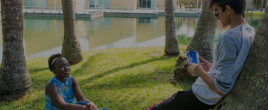 A female and male student sitting outside by a lake